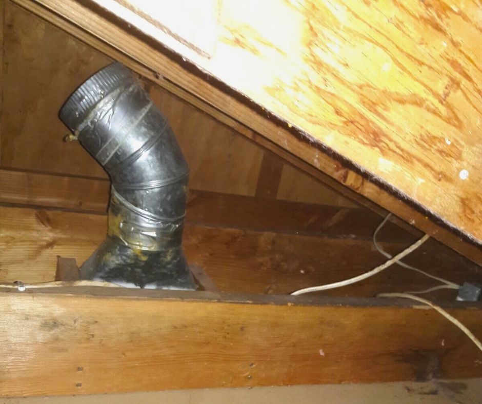 Bent metal vent pipe sealed with duct tape, installed between wooden beams in an attic