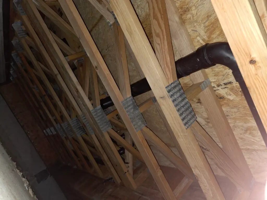 Black plumbing pipe routed through open web floor joists in an uninsulated crawl space