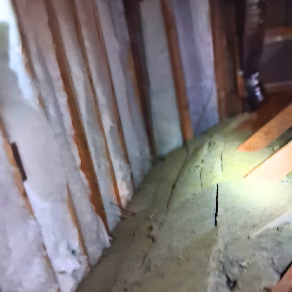 Insulation work inside a real San Rafael attic — wooden studs with batts and cellulose under flashlight